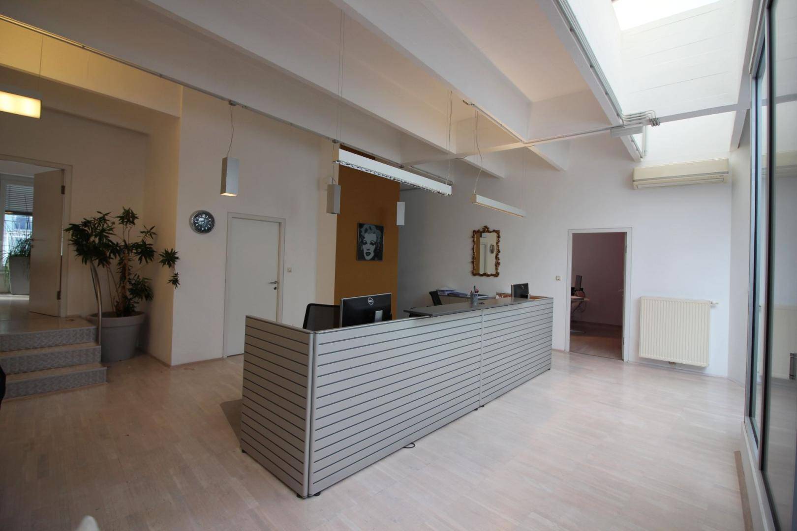 Moderner Empfangsbereich mit Schreibtisch, Pflanzen und hellen Holzböden, ideal für Büronutzung.