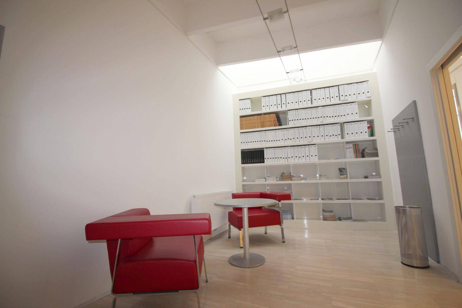 Kleiner Wartebereich mit roten Sesseln und einem Bücherregal, bietet eine gemütliche Atmosphäre.