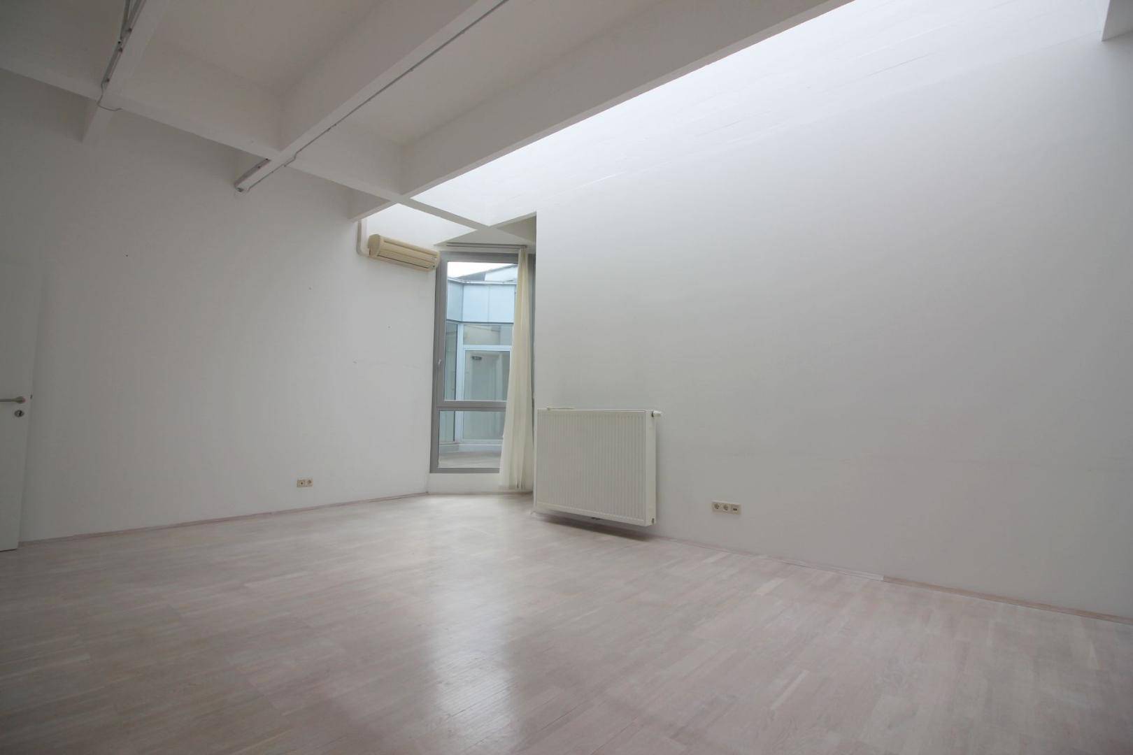 Heller Raum mit Holzboden, einem Fenster und einem Heizkörper, der viel Tageslicht hereinlässt.