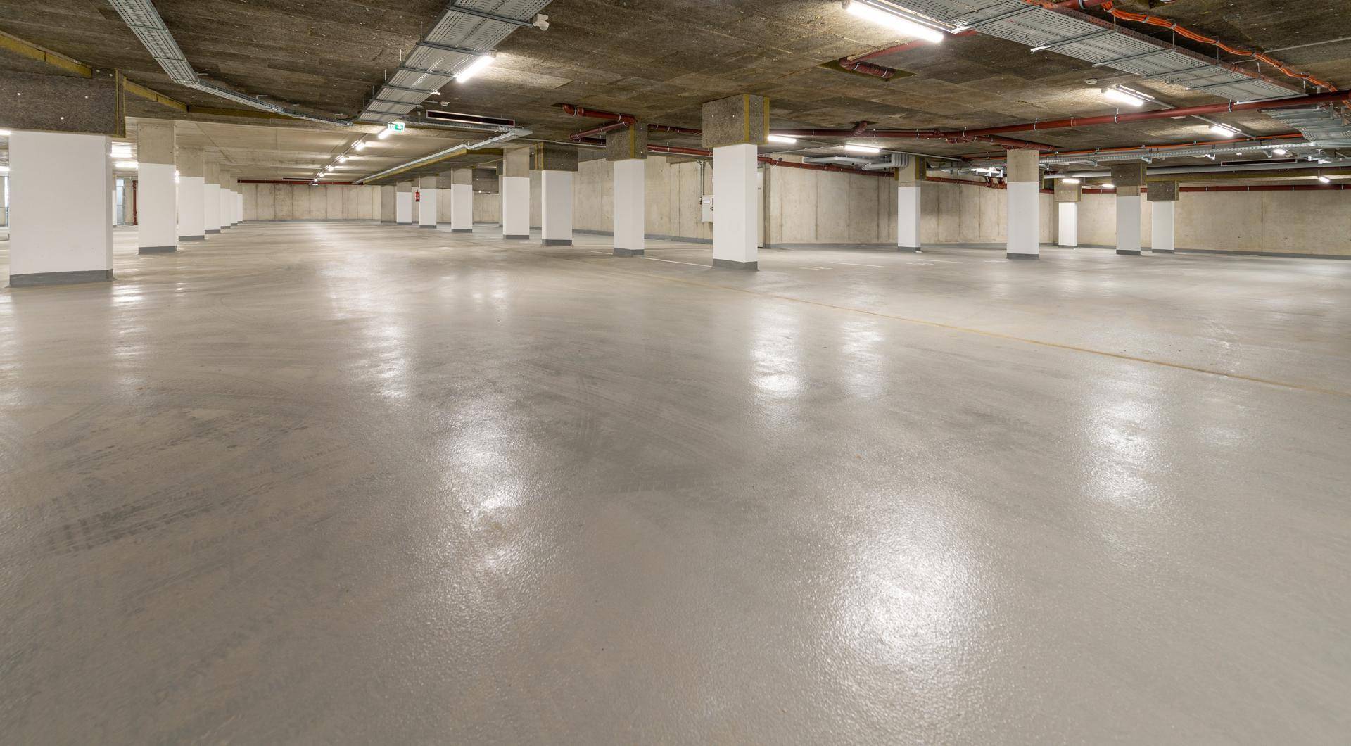 Geräumige und helle Tiefgarage mit zahlreichen Stellplätzen und Betonboden.