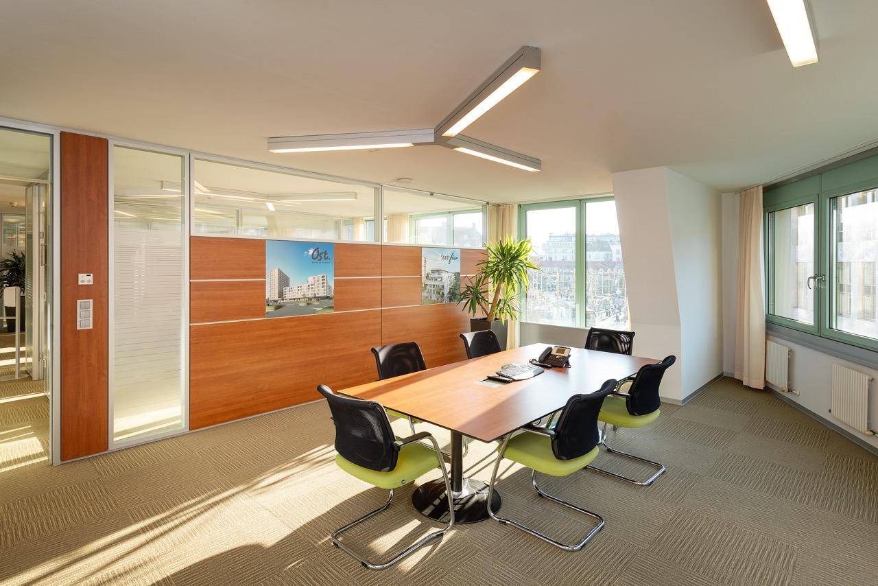 Moderner Konferenzraum mit großem Holztisch, ergonomischen Stühlen und viel Tageslicht.