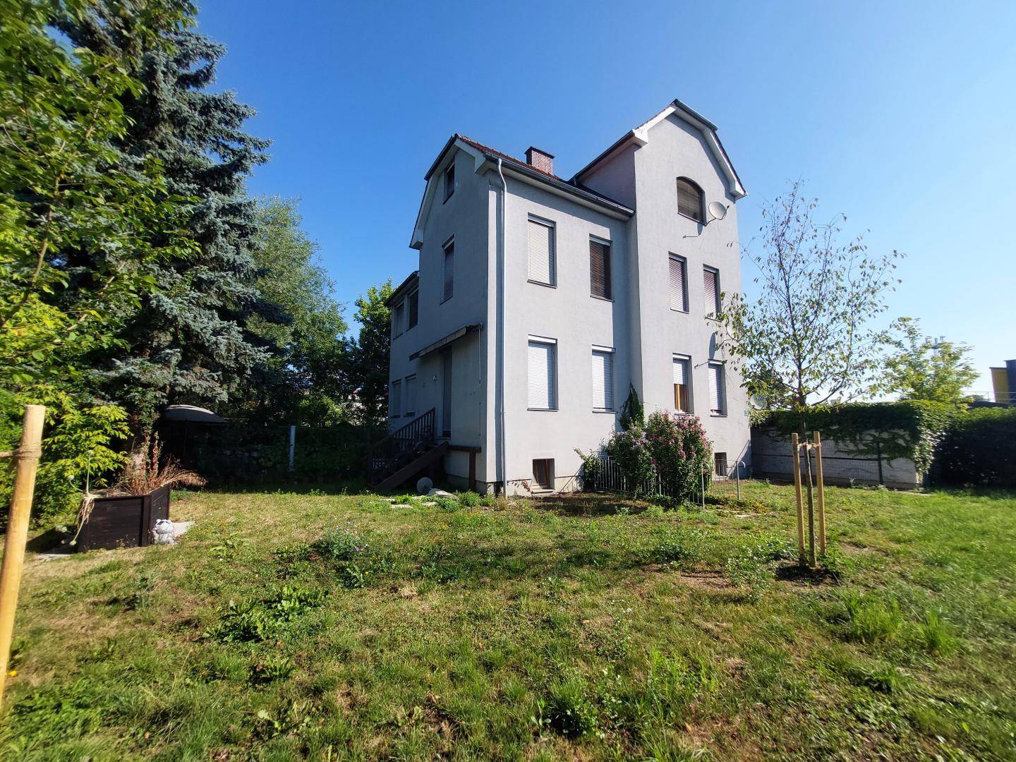 Seitenansicht des Gebäudes mit großem Gartenbereich und altem Baumbestand.