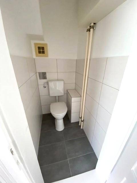 Kleines WC mit weißer Toilette und grauen Bodenfliesen.