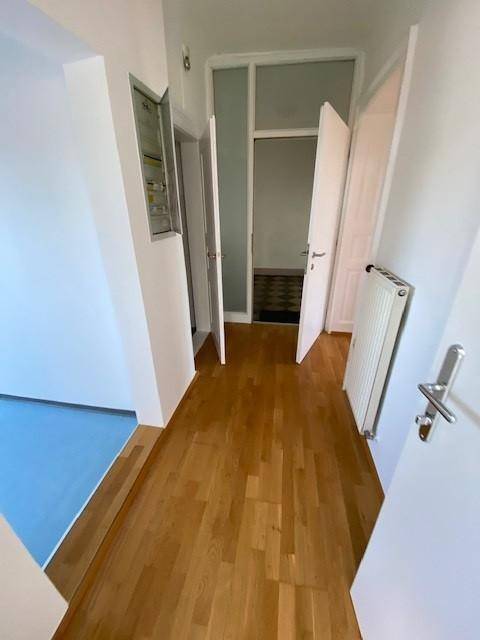Heller Flur mit Holzparkettboden, weißen Wänden und mehreren Türen.