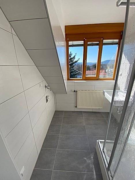 Modern gefliestes Badezimmer mit Dusche, Waschbecken und Fenster unter einer Dachschräge.