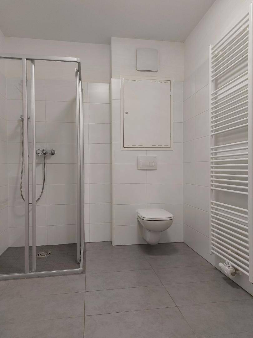 Helles Badezimmer mit moderner Duschkabine, wandhängendem WC, Fliesenboden und beheiztem Handtuchhalter.