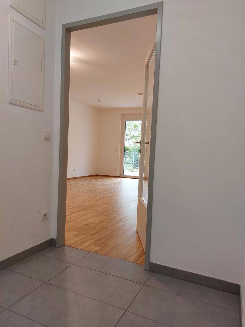 Blick vom Flur in einen hellen Raum mit Holzboden und Zugang zum Balkon.
