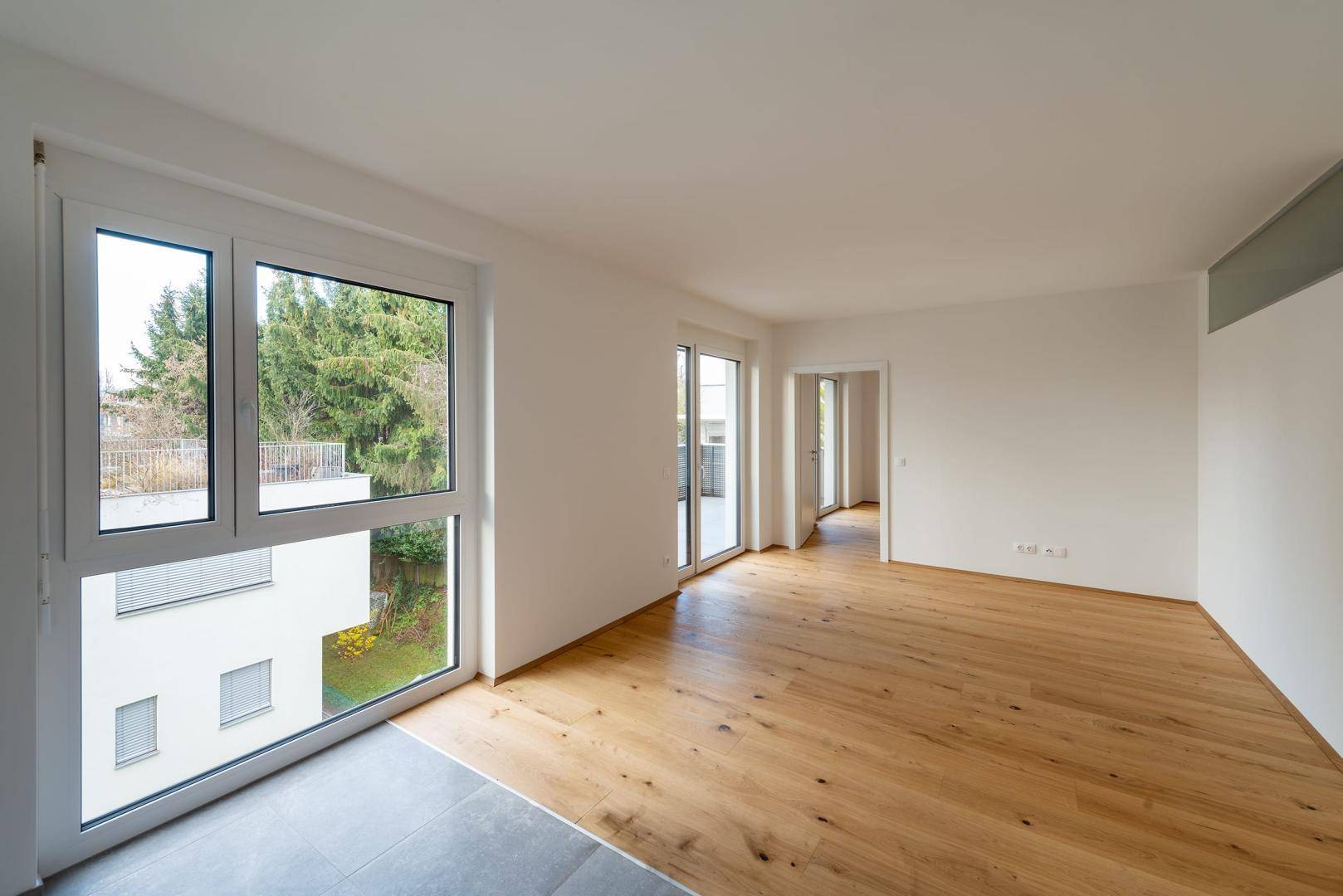Lichtdurchfluteter Wohnraum mit Holzboden, großen Fenstern und Blick ins Grüne.