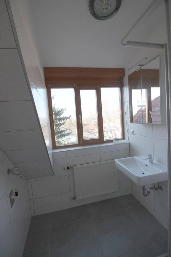 Helles Badezimmer im Dachgeschoss mit Fenster, Waschbecken und weißen Fliesen.