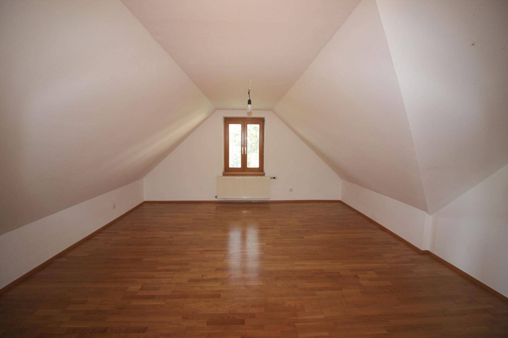 Heller Dachbodenraum mit schrägen Wänden, Holzboden und einem Fenster für Tageslicht.