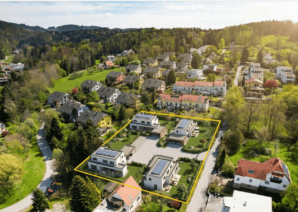 Luftaufnahme einer modernen Wohnsiedlung mit mehreren Häusern und umgebender grüner Landschaft.