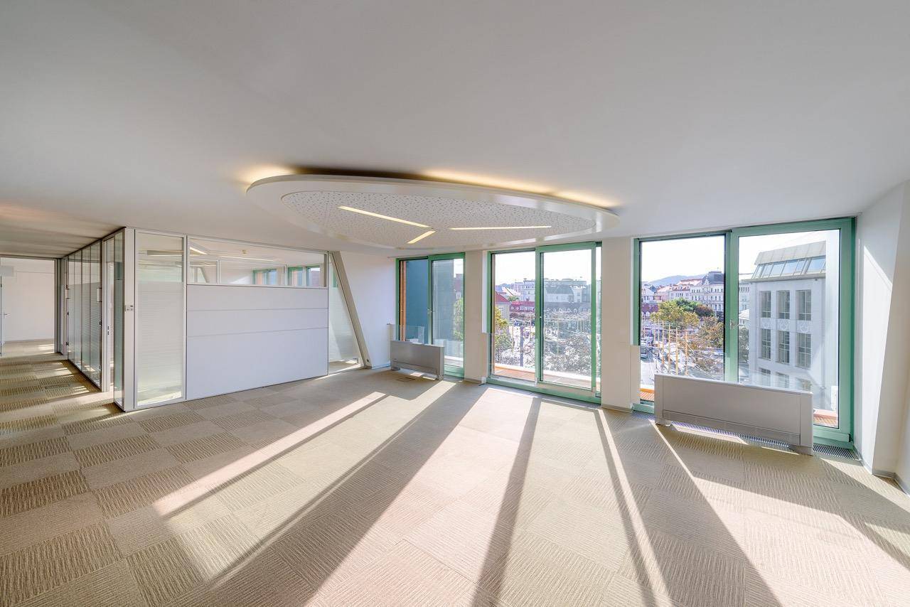 Geräumiges, leeres Büro mit Teppichboden, Glaswänden und großen Fenstern mit Stadtblick.