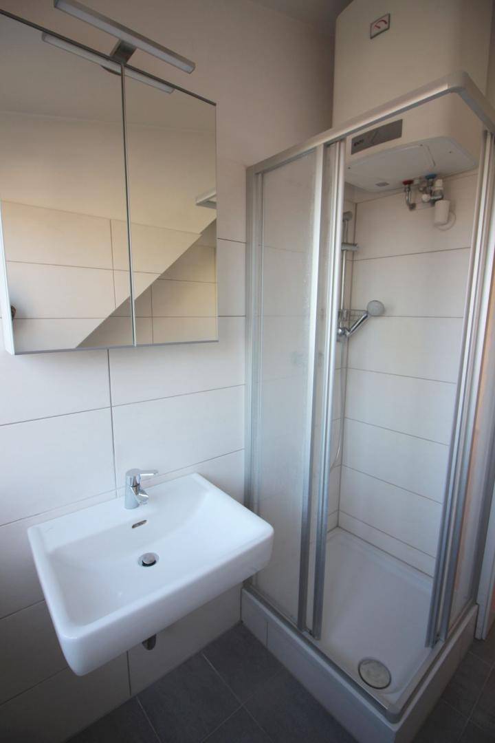 Modernes Badezimmer mit Duschkabine, Waschbecken und Spiegelschrank, hell gefliest.