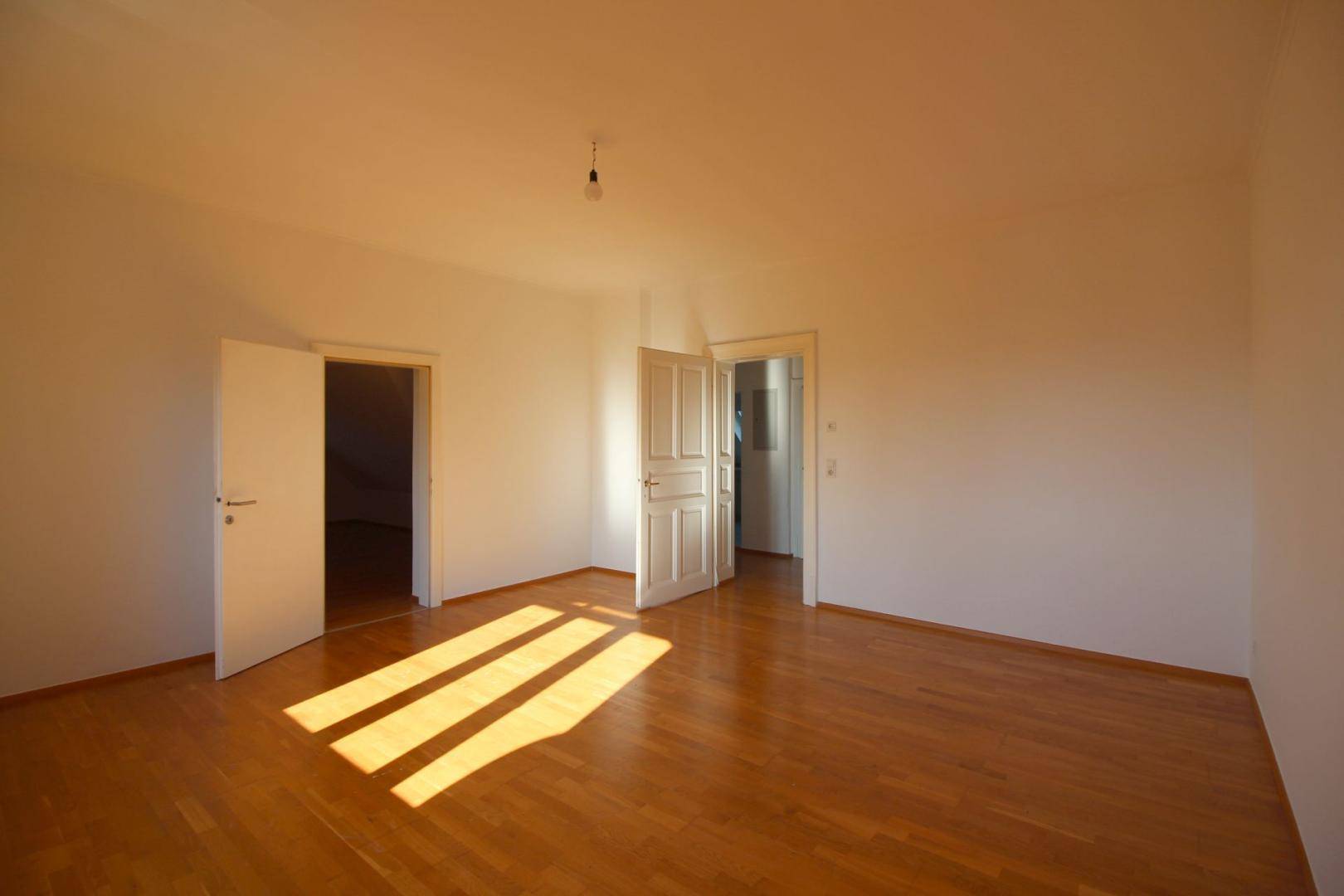 Geräumiges Zimmer mit Holzboden und zwei offenen Türen, das viel natürliches Licht empfängt.