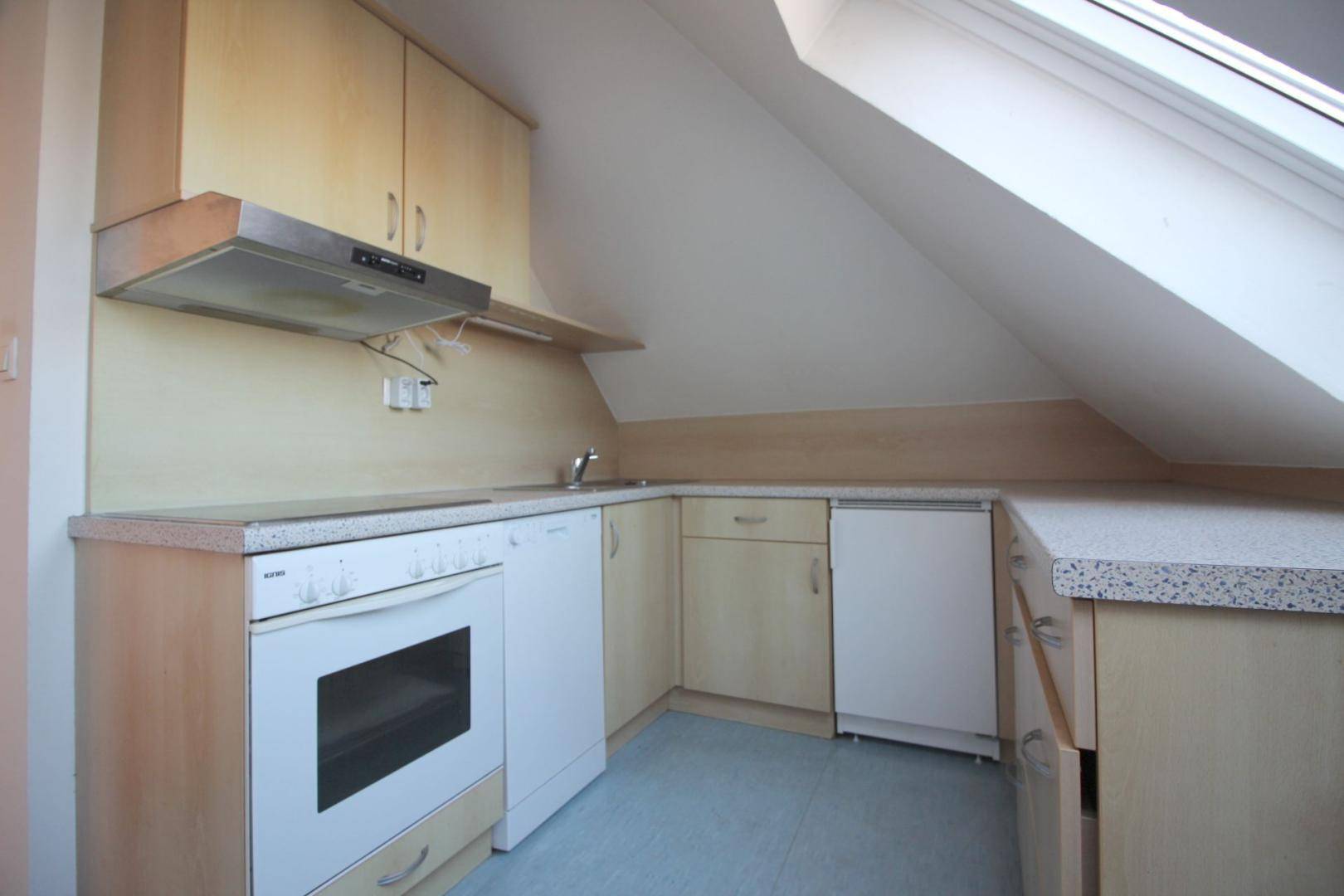 Kleine Küche im Dachgeschoss mit Einbauschränken, Backofen und einem Dachfenster für natürliches Licht.