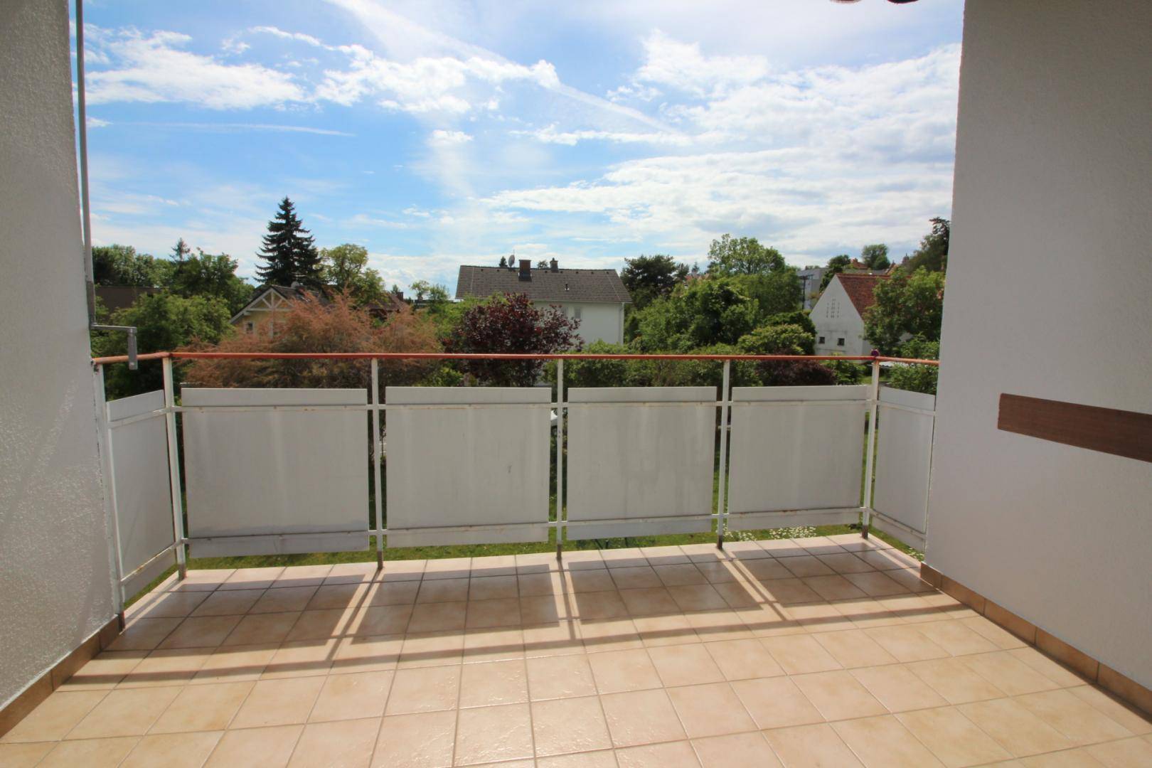 Geräumiger Balkon mit Fliesenboden und Blick auf eine grüne Wohngegend.