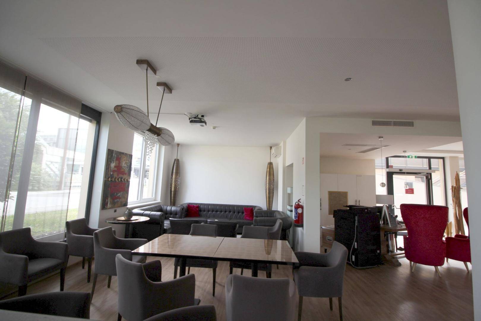 Gemütlicher Loungebereich mit dunklem Sofa, Esstisch und großen Fenstern für viel Tageslicht.