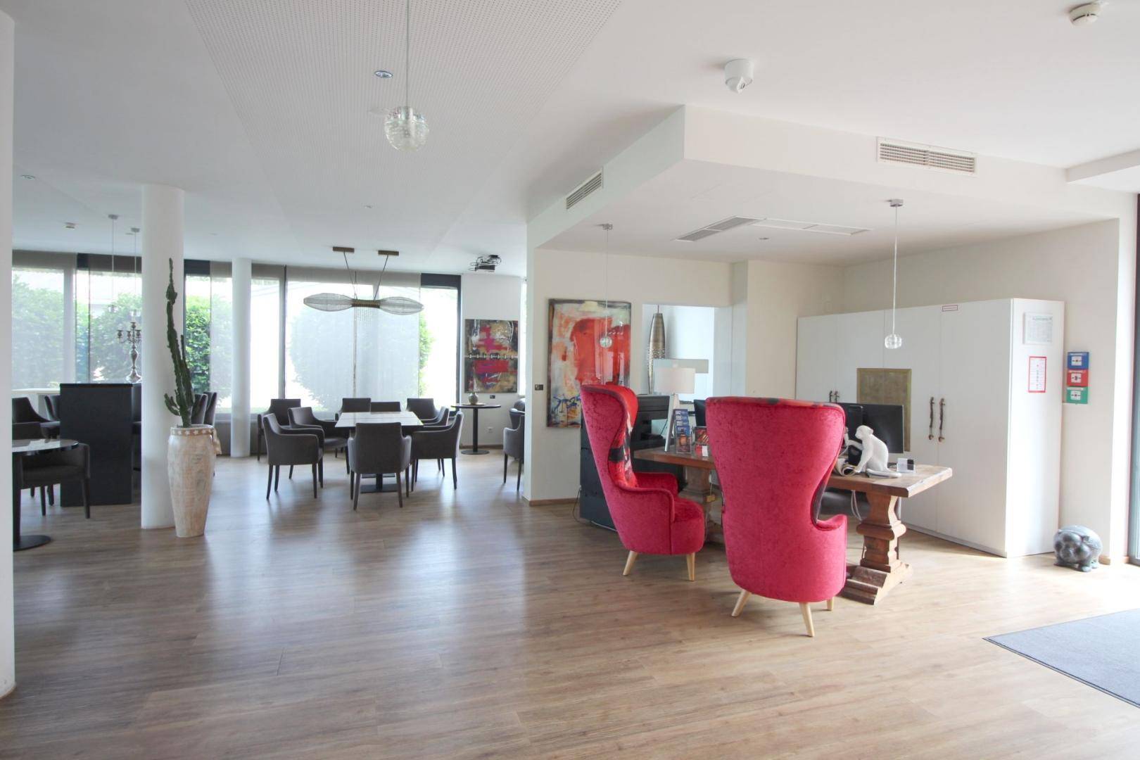 Heller Loungebereich mit Sitzgelegenheiten, Holzboden und einem Essbereich im Hintergrund.