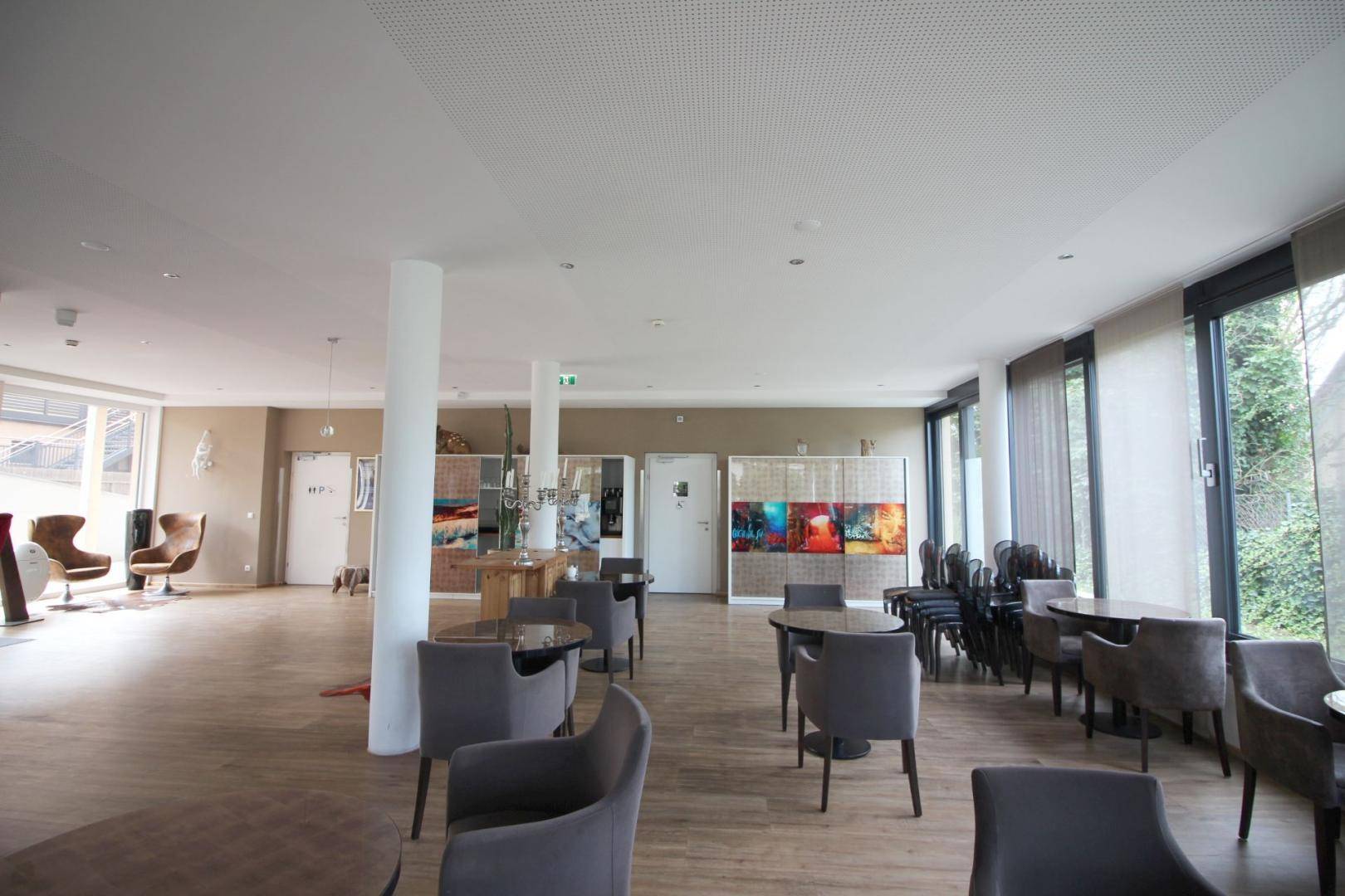 Weiter Loungebereich mit verschiedenen Sitzgruppen, Holzboden und großen Fenstern.