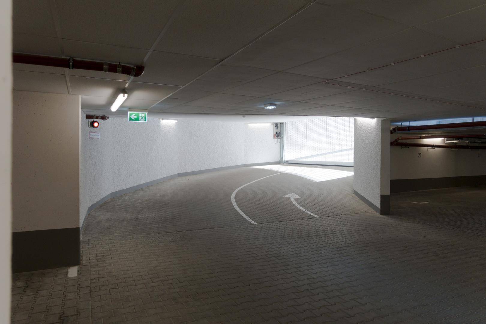 Helle und saubere Zufahrt zur Tiefgarage mit Pfeilmarkierungen auf dem Boden.