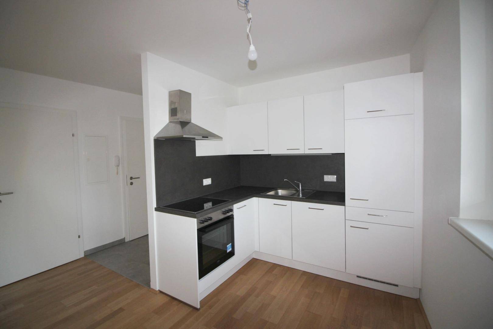Moderne, kompakte Einbauküche mit weißen Schränken und dunkler Arbeitsplatte.