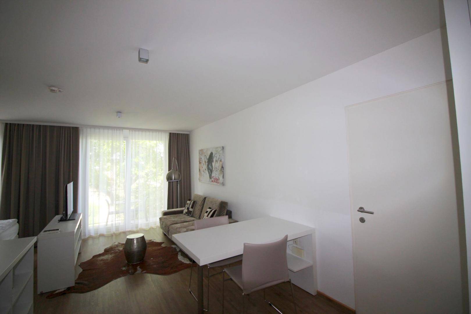 Gemütlicher Wohnbereich mit Esstisch, Sofa und großen Fenstern mit Blick ins Grüne.