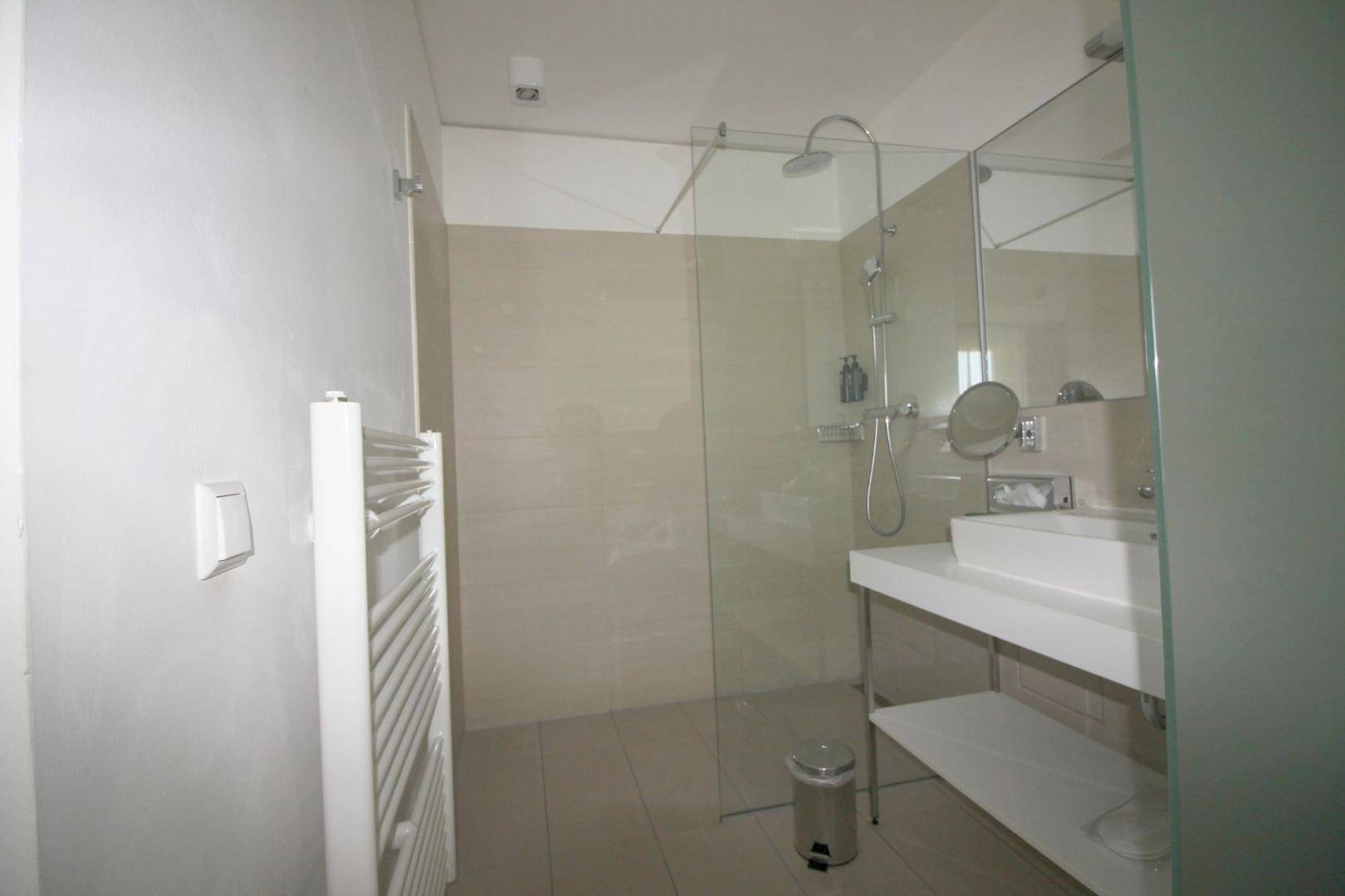 Modernes Badezimmer mit ebenerdiger Dusche, Einzelwaschbecken und beheiztem Handtuchhalter.