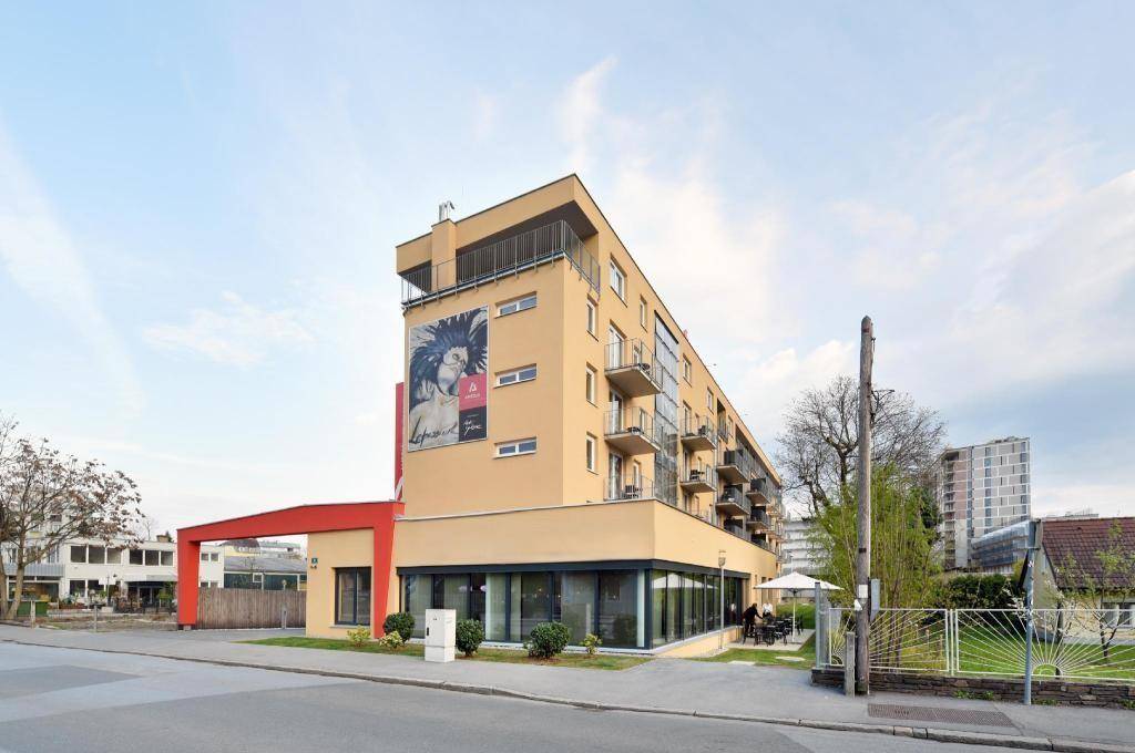 Modernes Gebäude mit markanter Architektur, großen Fenstern und mehreren Balkonen an einer Straße.