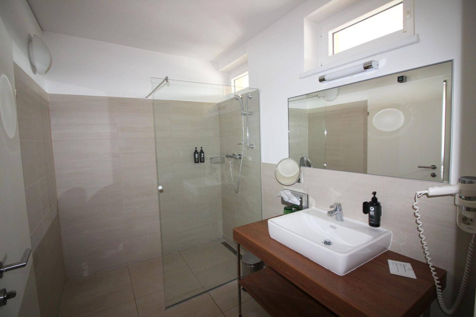 Modernes Badezimmer mit ebenerdiger Dusche, Einzelwaschbecken und einem kleinen Fenster.