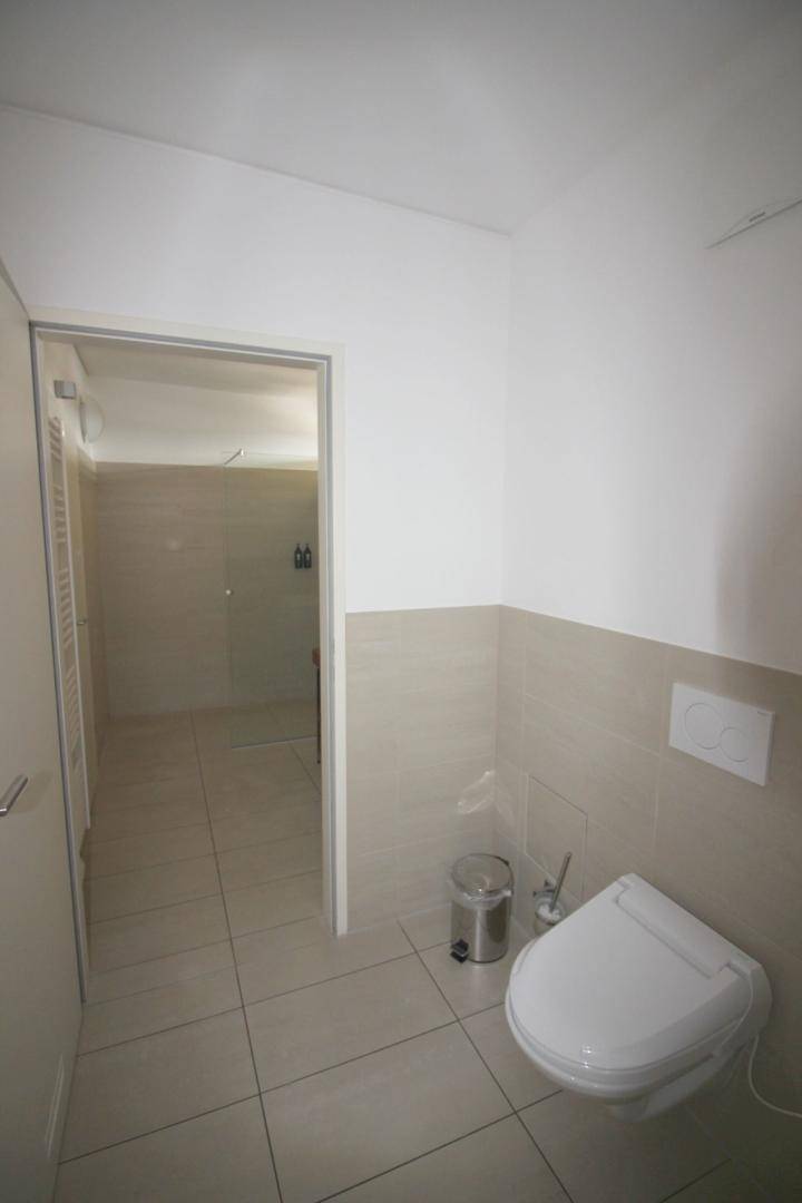 Separates WC mit wandhängender Toilette und Fliesenboden, angrenzend an den Duschbereich.