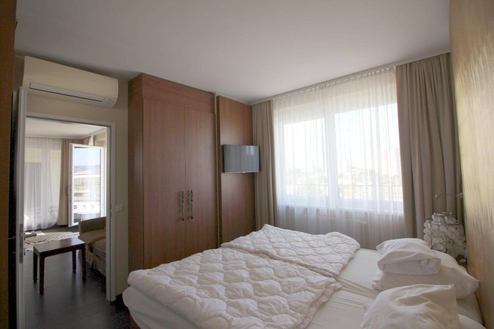 Schlafzimmer mit Einbauschrank, Wandfernseher und großem Fenster, das viel Helligkeit bietet.