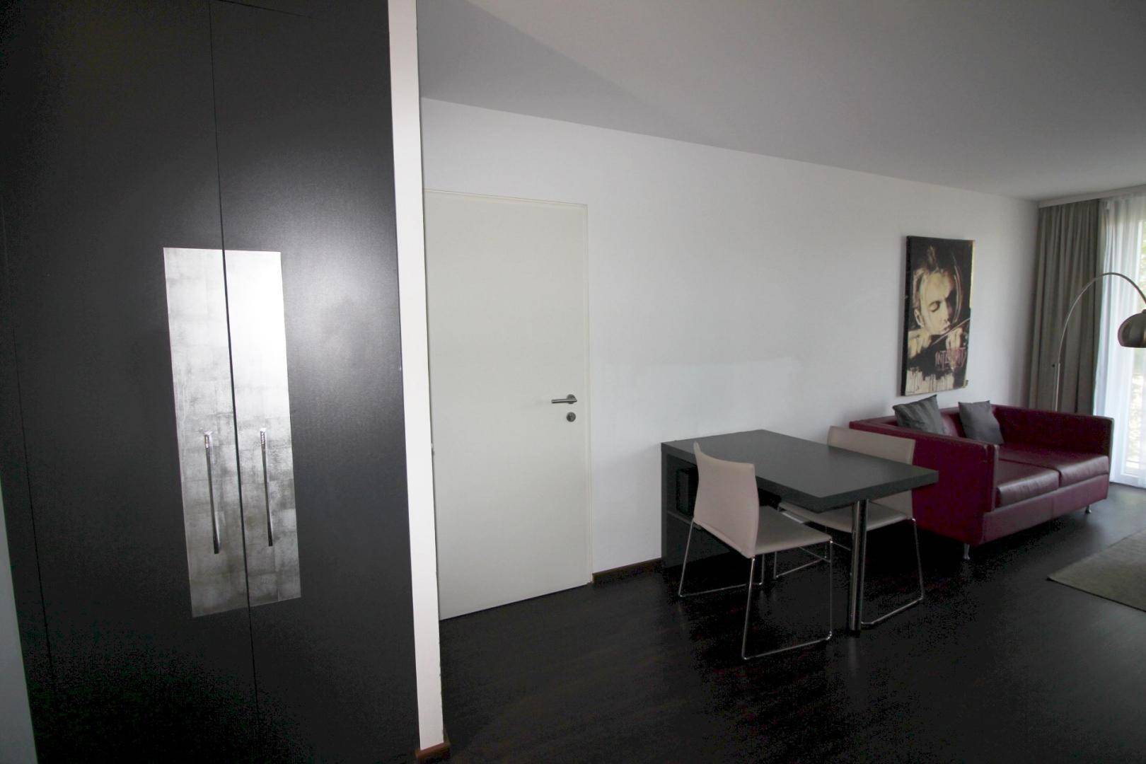 Wohnbereich mit Esstisch, rotem Sofa und integriertem Kleiderschrank in der Studio-Wohnung.