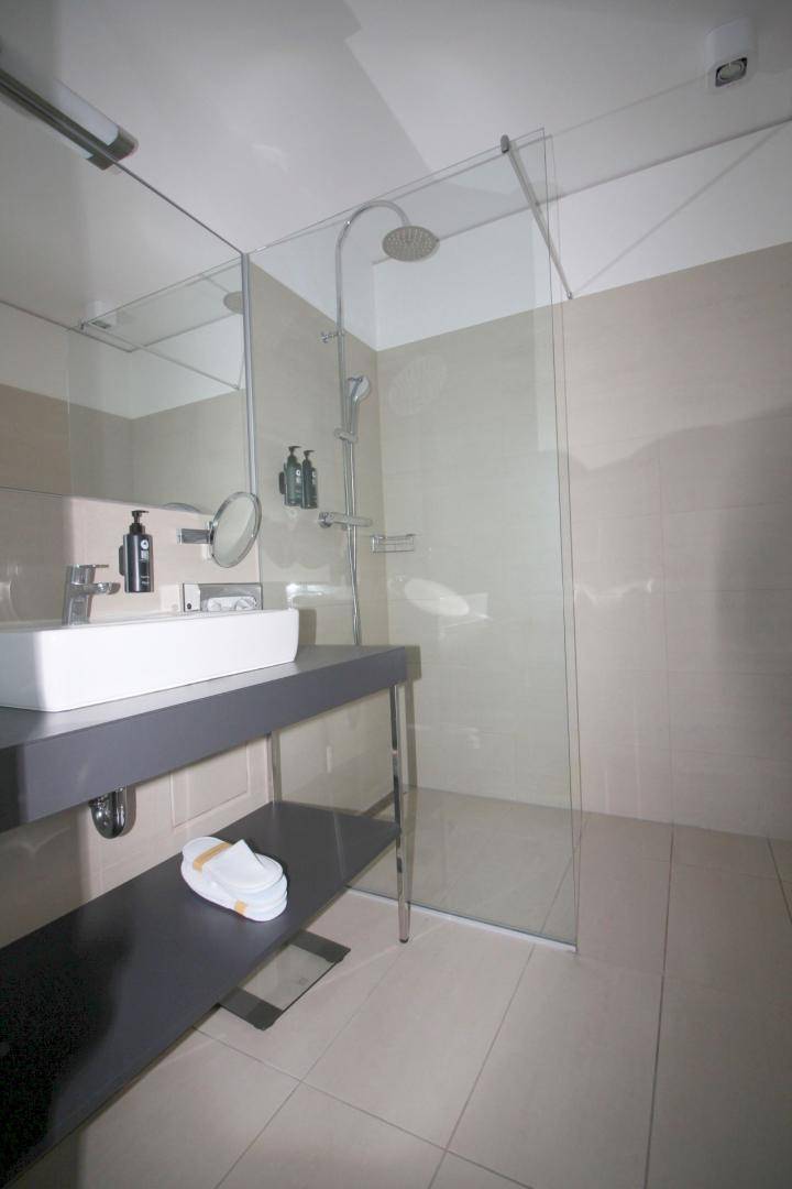 Modernes Badezimmer mit begehbarer Dusche, Einzelwaschbecken und hellen Fliesen.