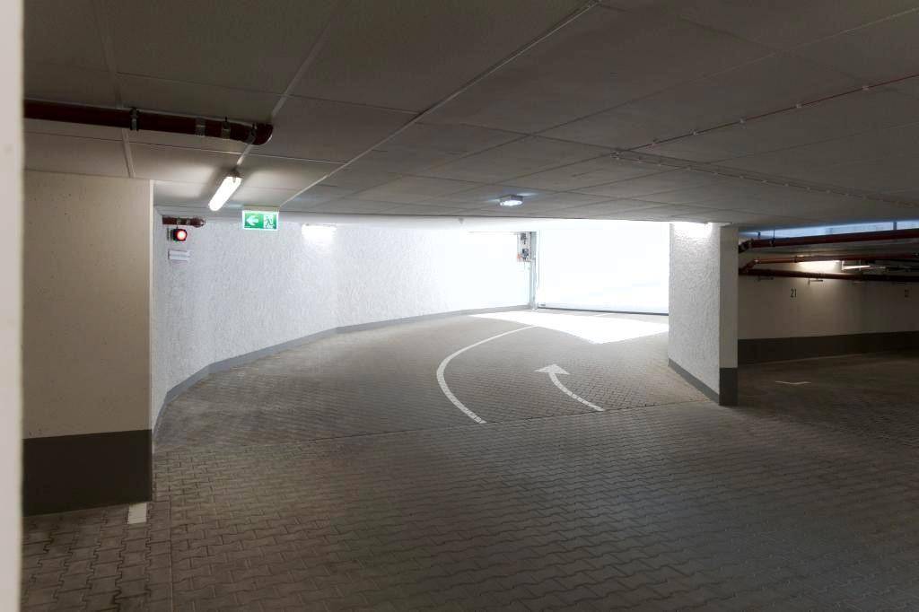 Einfahrt zu einer Tiefgarage mit Rampe, Betonboden und heller Beleuchtung.