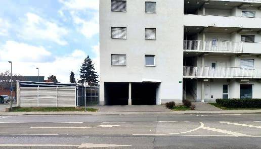 Weiße Wohnhausfassade von der Straße aus gesehen mit Garageneinfahrten und Fahrradschuppen.