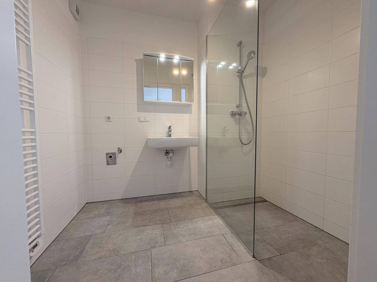 Modernes Badezimmer mit ebenerdiger Glasdusche, weißen Fliesen und einem praktischen Handtuchheizkörper.