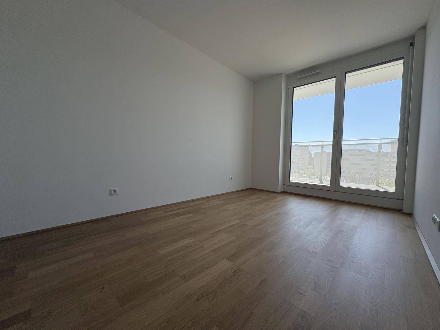 Geräumiges, helles Schlafzimmer mit Holzboden und großen Fenstern, die viel Tageslicht hereinlassen.