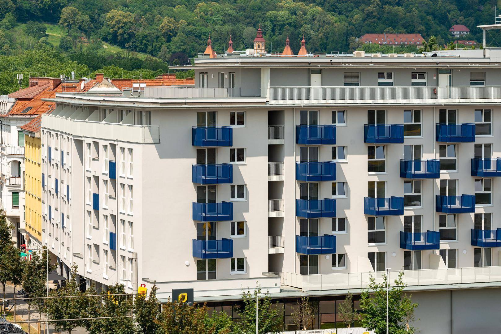 Moderne Wohnanlage mit blauen Balkonen und vielen Fenstern in einer städtischen Umgebung.