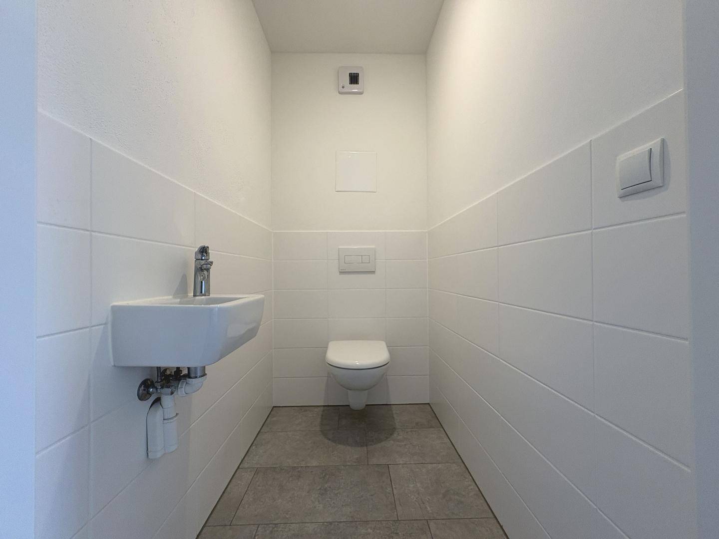 Separates Gäste-WC mit wandhängender Toilette, kleinem Waschbecken und weißen Fliesen.