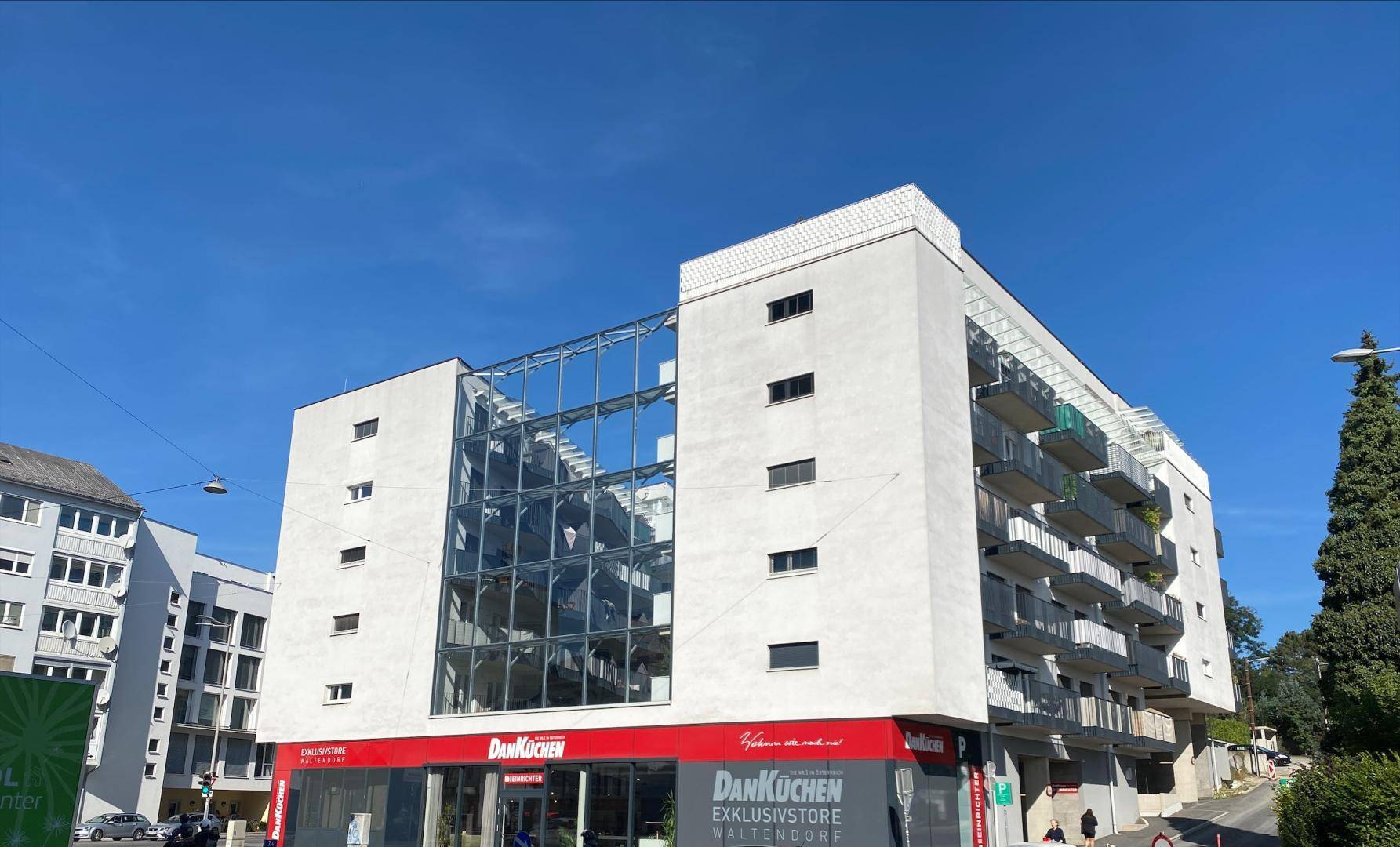 Modernes Gebäude mit markanter Glasfassade und Balkonen unter blauem Himmel.