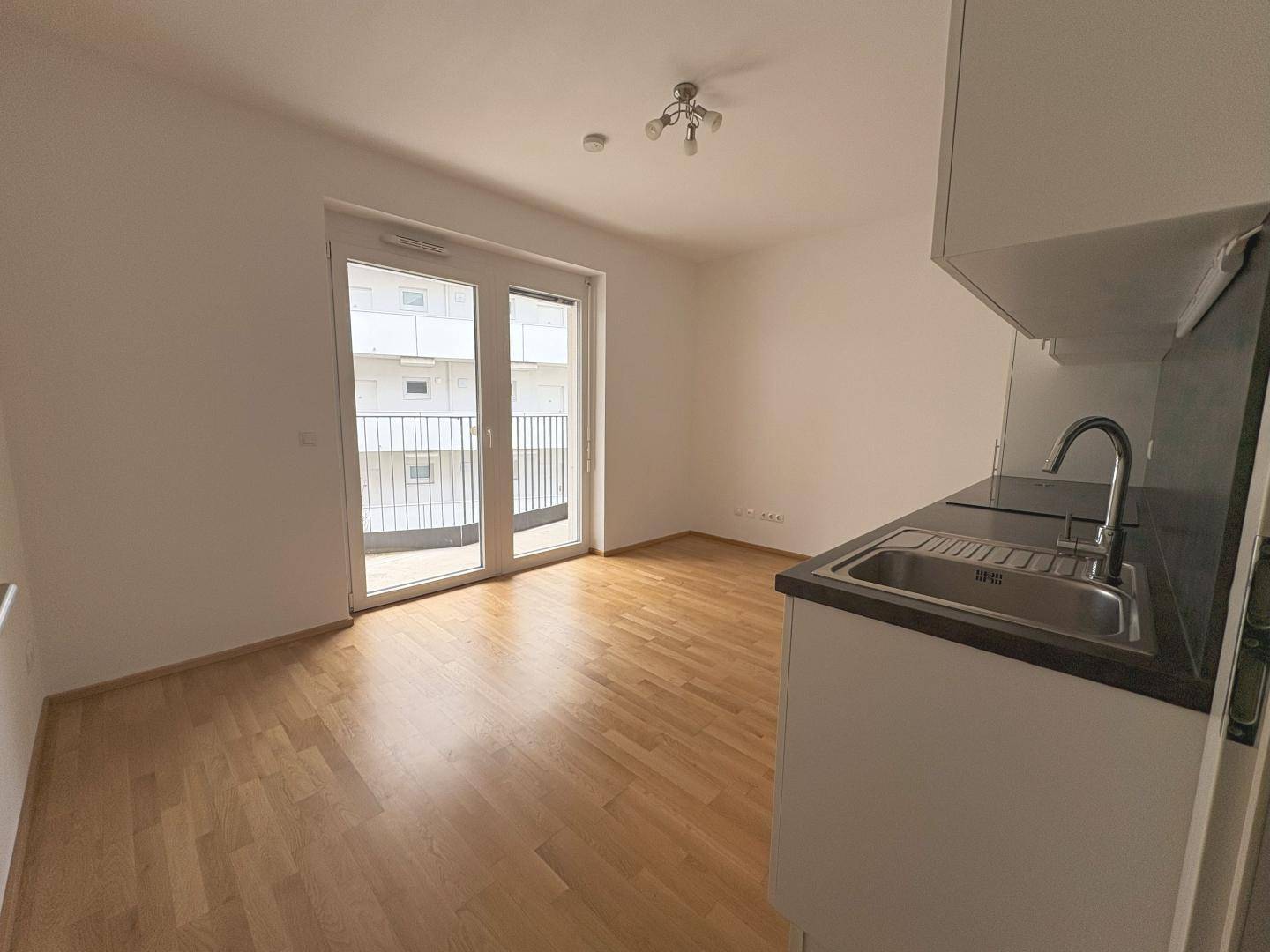 Lichtdurchfluteter Wohnbereich mit Holzboden und Zugang zu einem Balkon durch eine große Glastür.