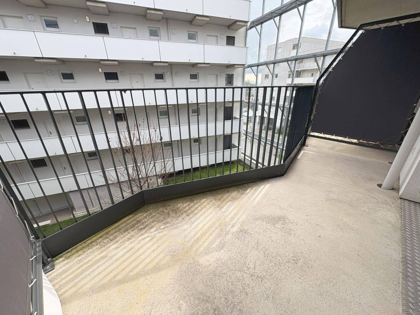 Balkon mit Blick auf den begrünten Innenhof eines modernen Wohnkomplexes.