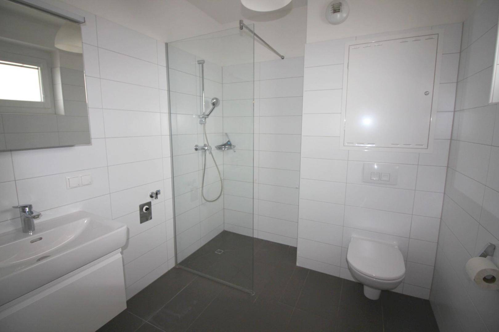 Modernes Badezimmer mit weißen Fliesen, ebenerdiger Dusche und wandhängendem WC.