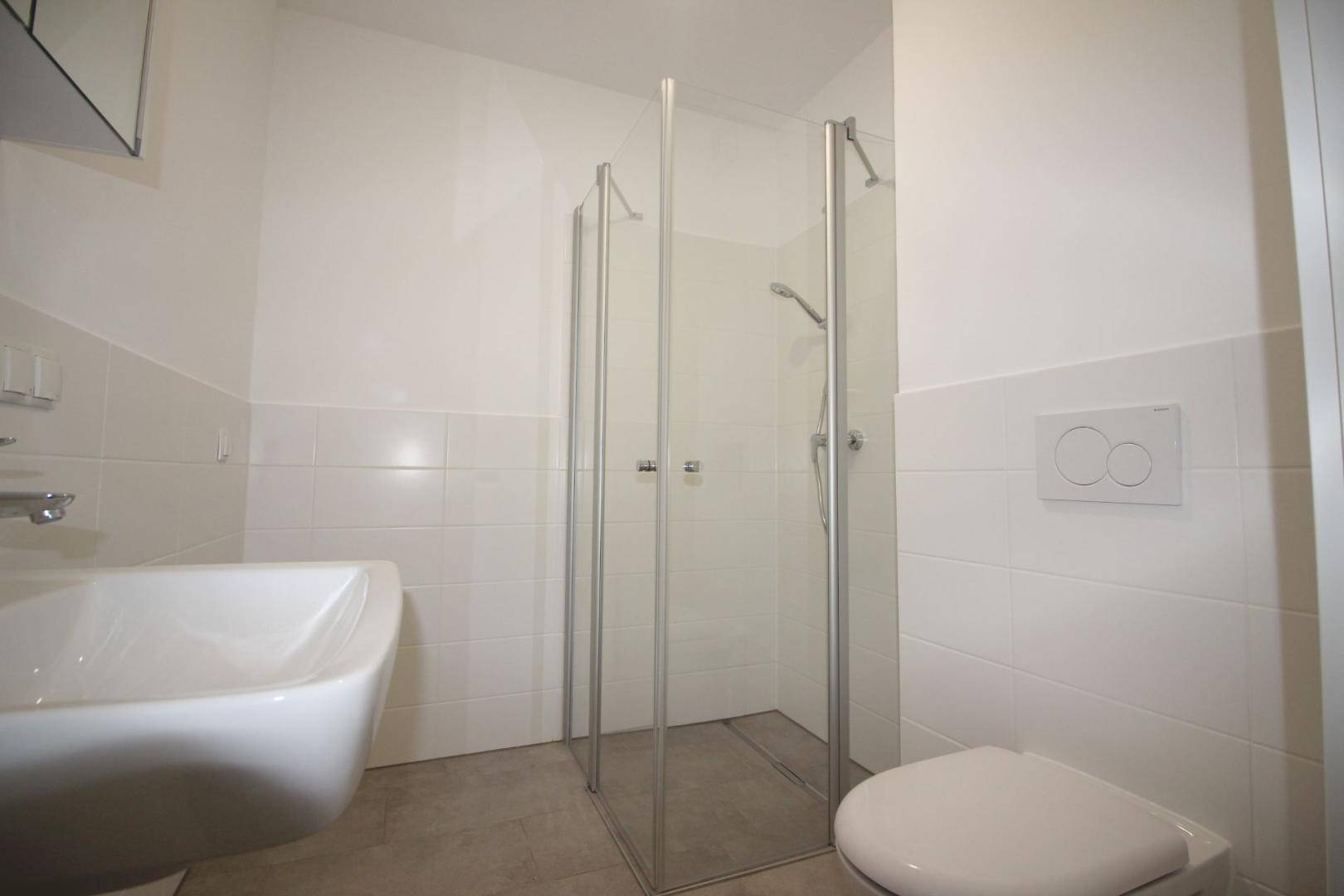 Funktionales Badezimmer mit Duschkabine, WC und hellen Fliesen an Wänden und Boden.