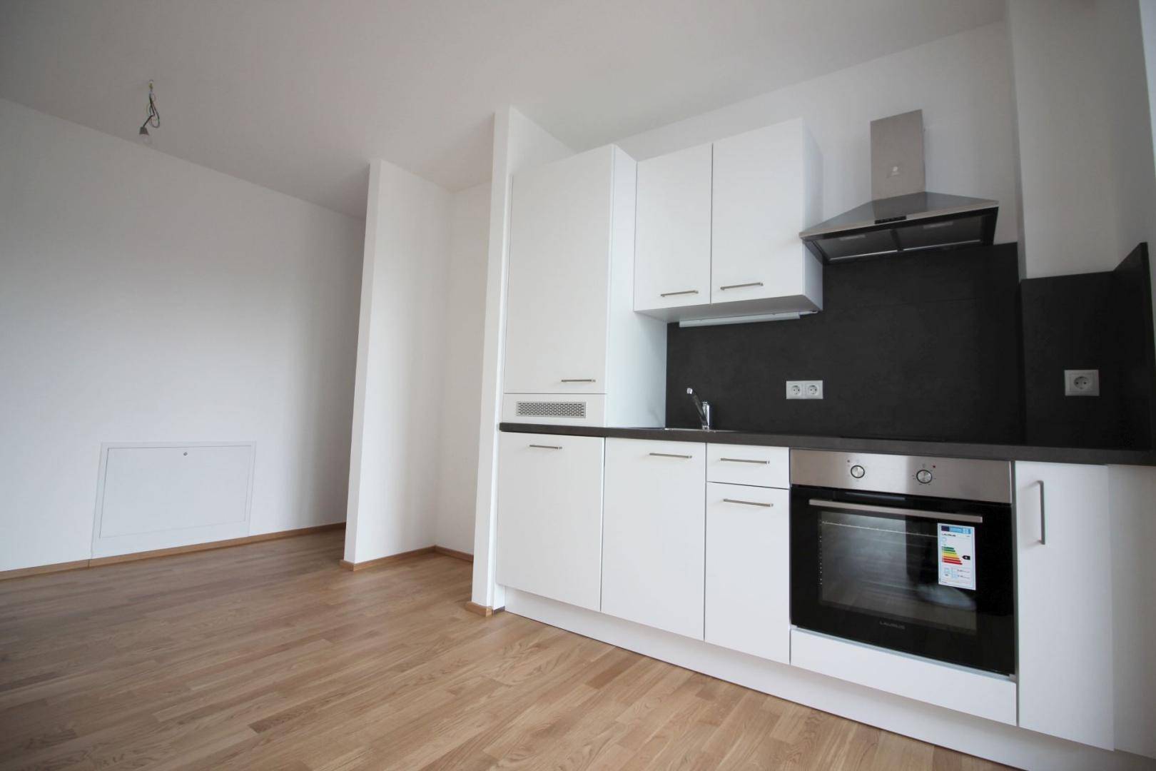 Moderne Küchenzeile mit weißen Schränken, dunkler Arbeitsplatte und integriertem Backofen.