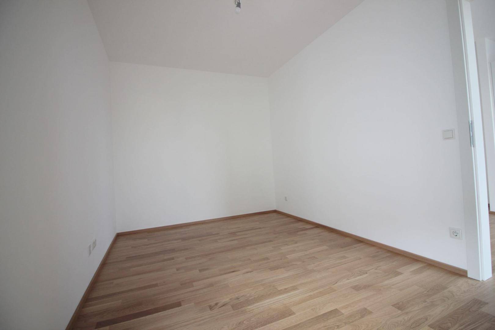 Leeres Zimmer mit hellem Parkettboden und weißen Wänden, ideal als Schlaf- oder Arbeitszimmer.