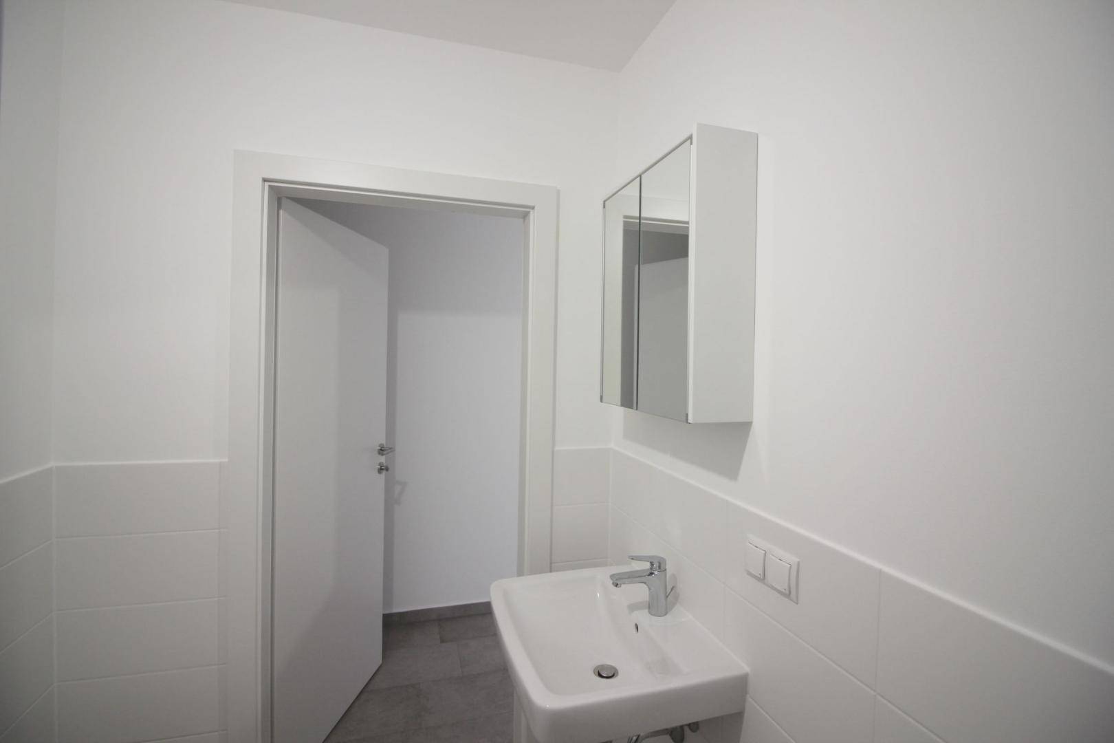 Modernes Badezimmer mit Waschbecken, Spiegelschrank und weißen Wandfliesen.
