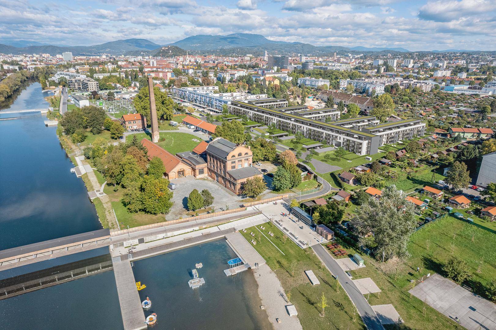 Luftaufnahme des Wohnkomplexes am Flussufer mit Stadt- und Bergblick.