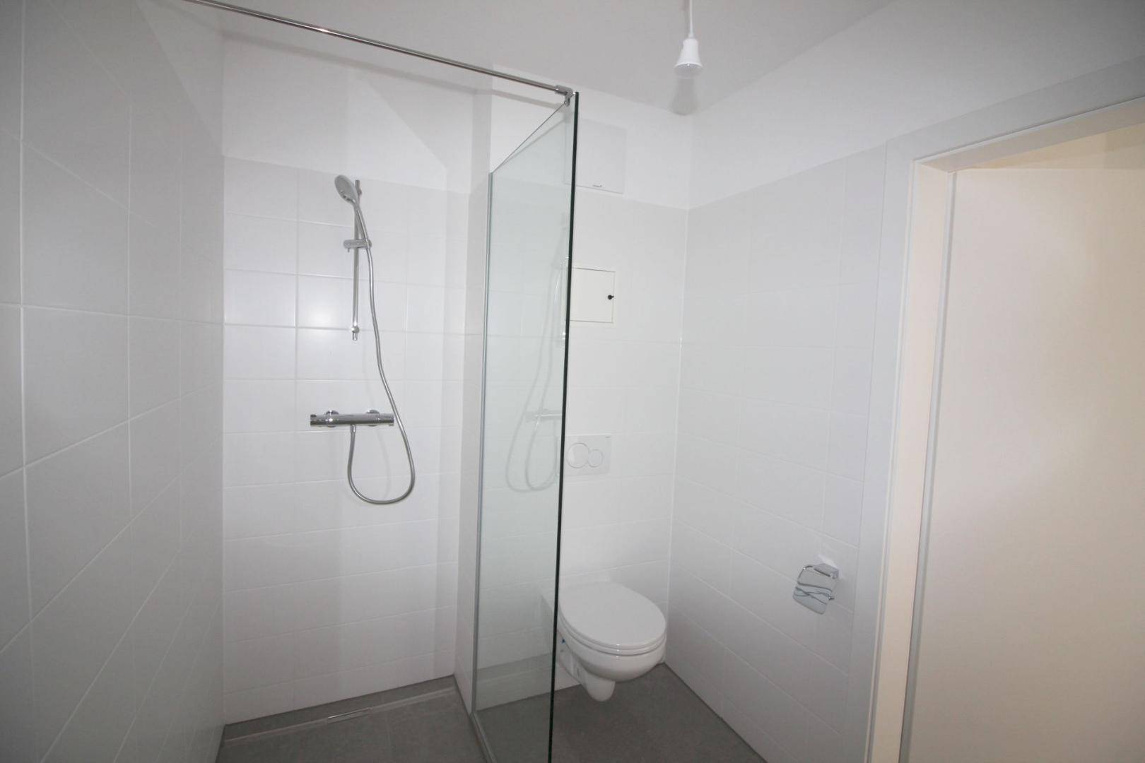 Funktionales Badezimmer mit ebenerdiger Dusche und wandhängendem WC.