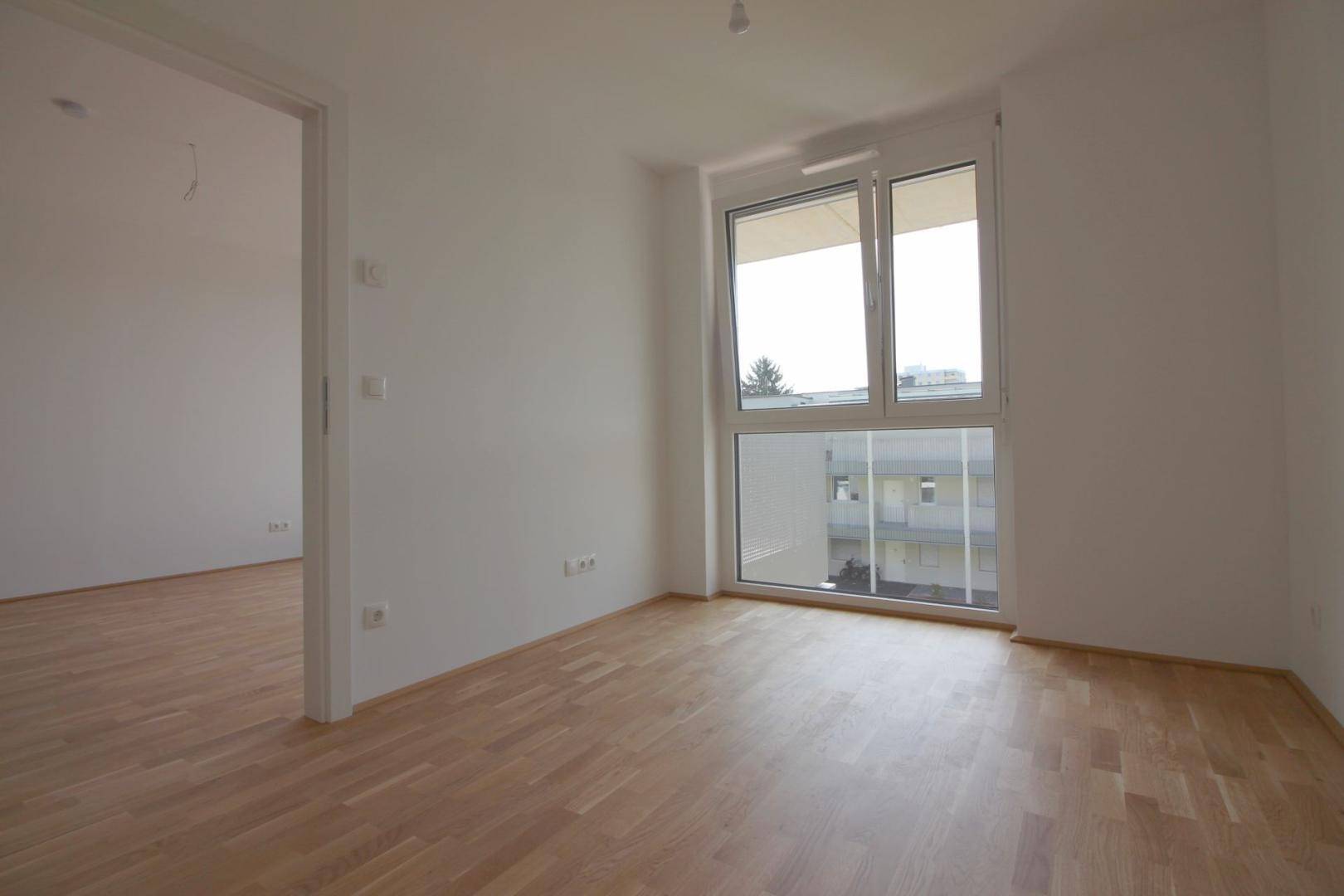 Helles Zimmer mit Parkettboden und großem Fenster, ideal als Schlaf- oder Arbeitszimmer.